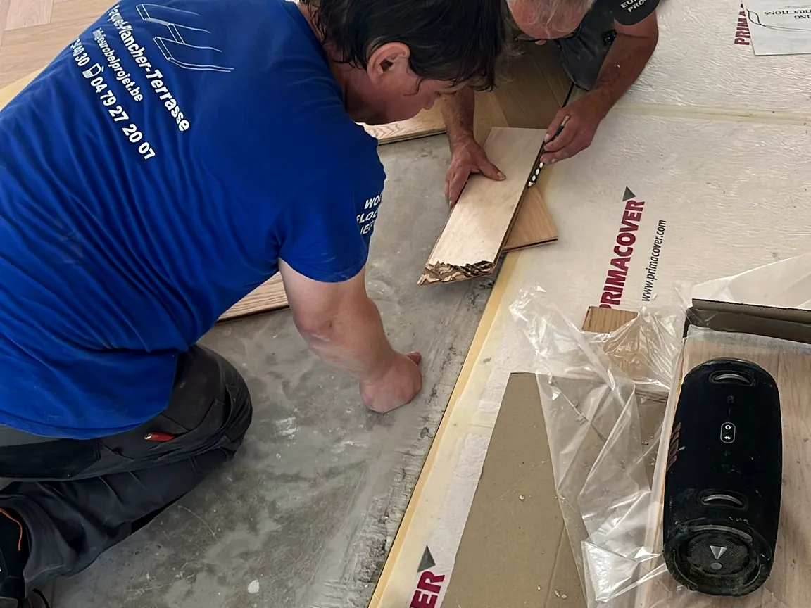 Deux poseurs Wood Floors ajustent une lame de rive du bâton rompu, chantier à Wemmel